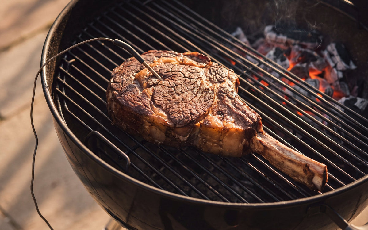 Côte de bœuf épaisse à l'os sur la grille d'un barbecue à couvercle, sonde à viande plantée à cœur
